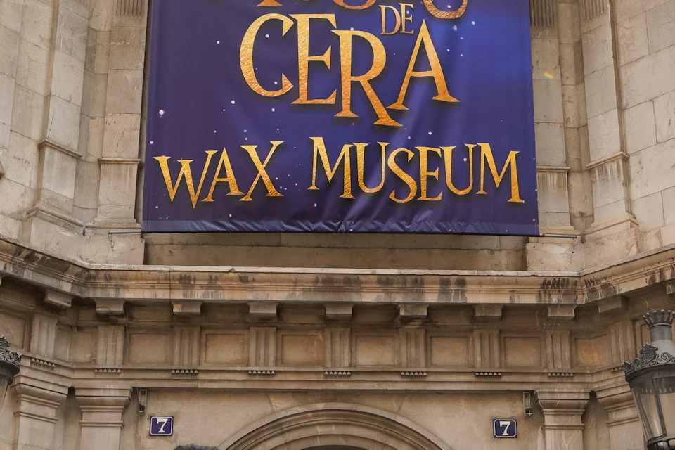 A family of four stands in front of a building with a sign reading 'Museu de Cera Wax Museum.' The building has ornate architecture.