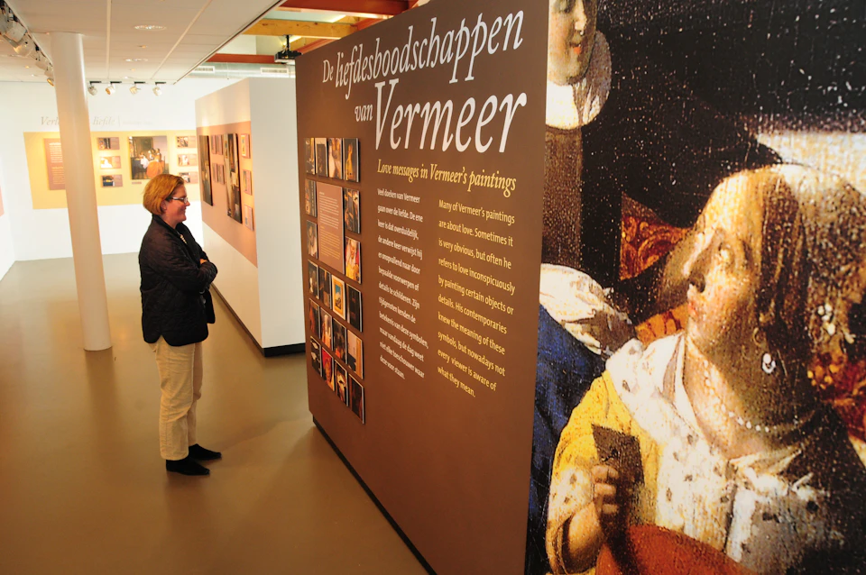 A person observes an exhibit panel titled "De liefdesboodschappen van Vermeer" with information and images about Vermeer's paintings.