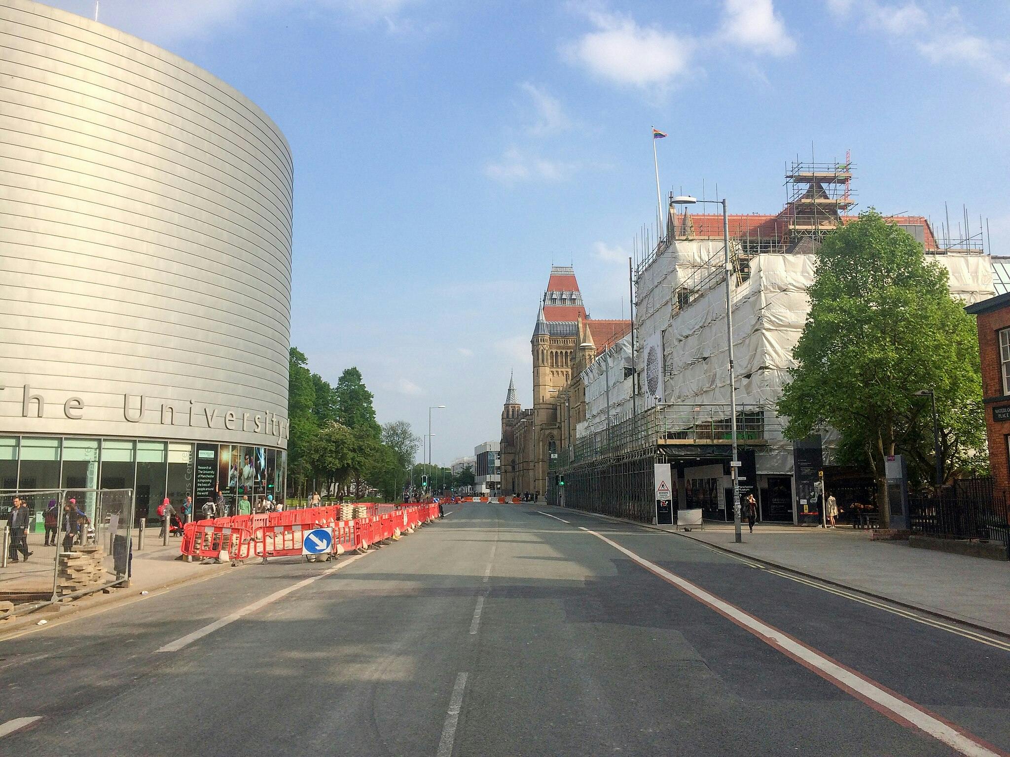 Vue de la rue avec un bâtiment cylindrique moderne, un bâtiment en cours d'échafaudage, une tour historique lointaine et un ciel bleu clair.