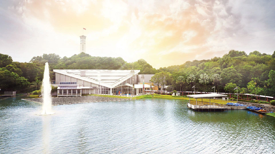 A scenic view of a waterfront area with modern buildings, trees, and a tower under a bright, partly cloudy sky.