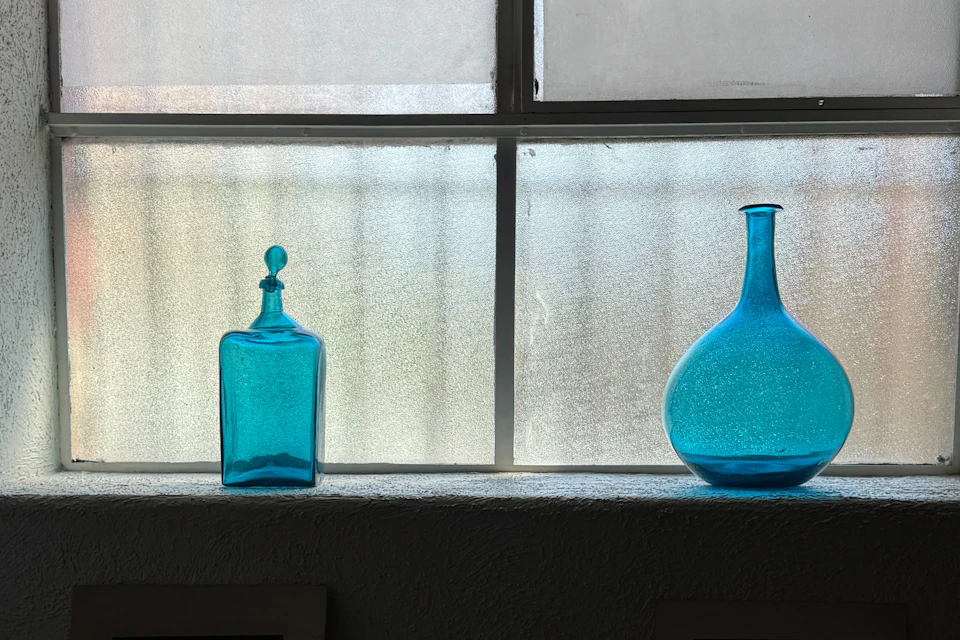 Two blue glass bottles sit on a windowsill against a frosted window with grid lines.