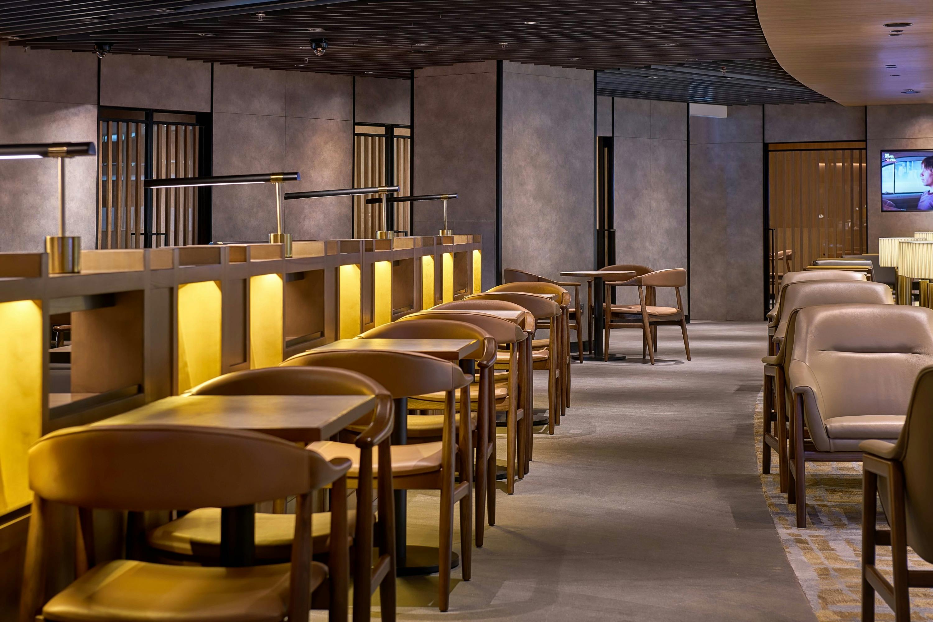 A modern, warmly lit interior of a restaurant with wooden tables and chairs arranged in rows, and a minimalist design.