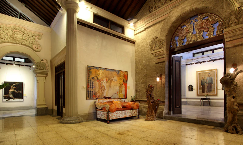 Indoor space with a patterned sofa, abstract painting, stone walls, an open arched doorway, and decorative lighting.