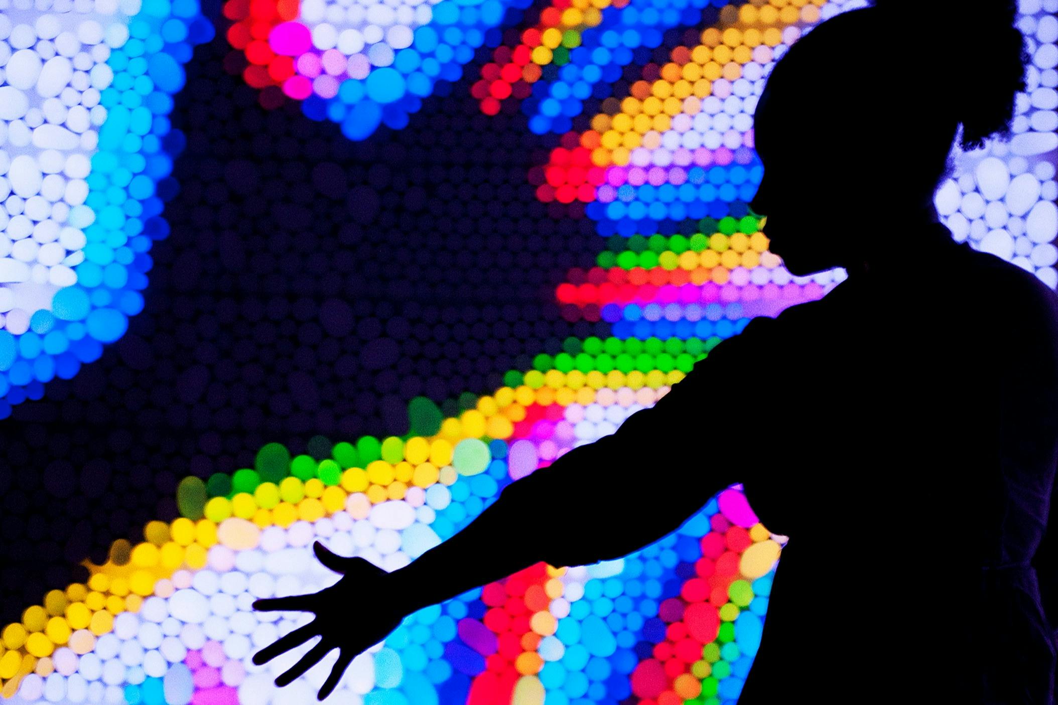Silhouette of a person reaching out against a vibrant, multicolored abstract light display.