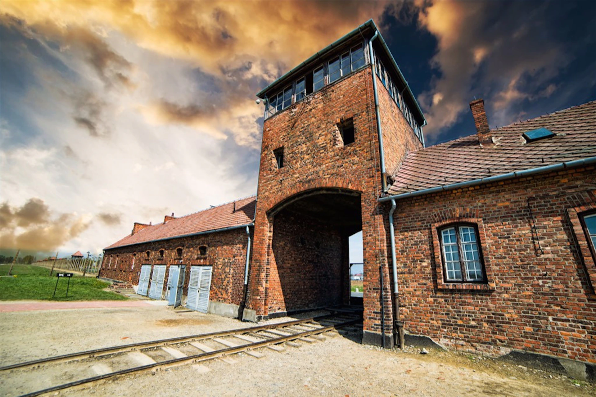 A brick building with an arched entrance and a rail track leading inside, set against a dramatic cloudy sky.