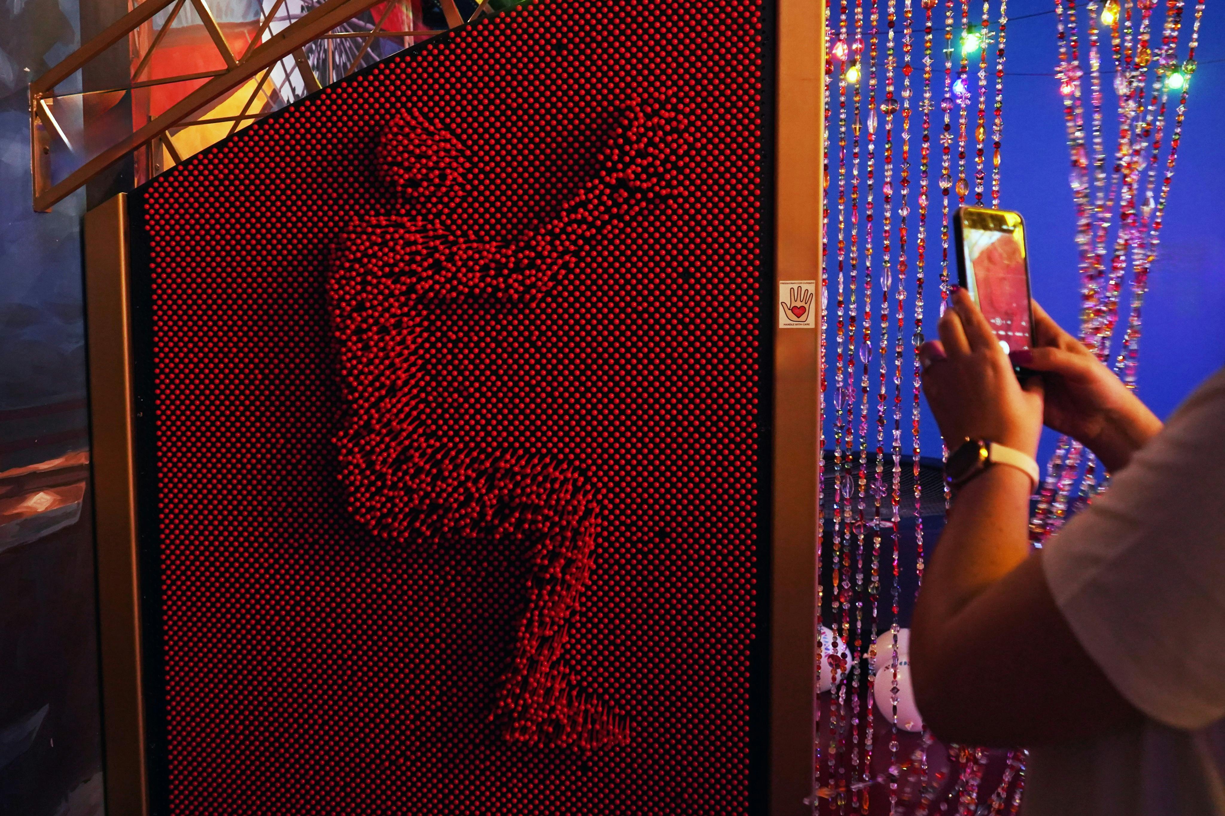 一幅红色图钉艺术板，描绘了一个坐姿的人形，附近有人在拍照。