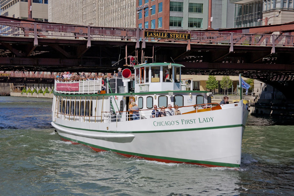 A white tour boat named "Chicago's First Lady" passes under La Salle Street bridge, with passengers on the open deck.