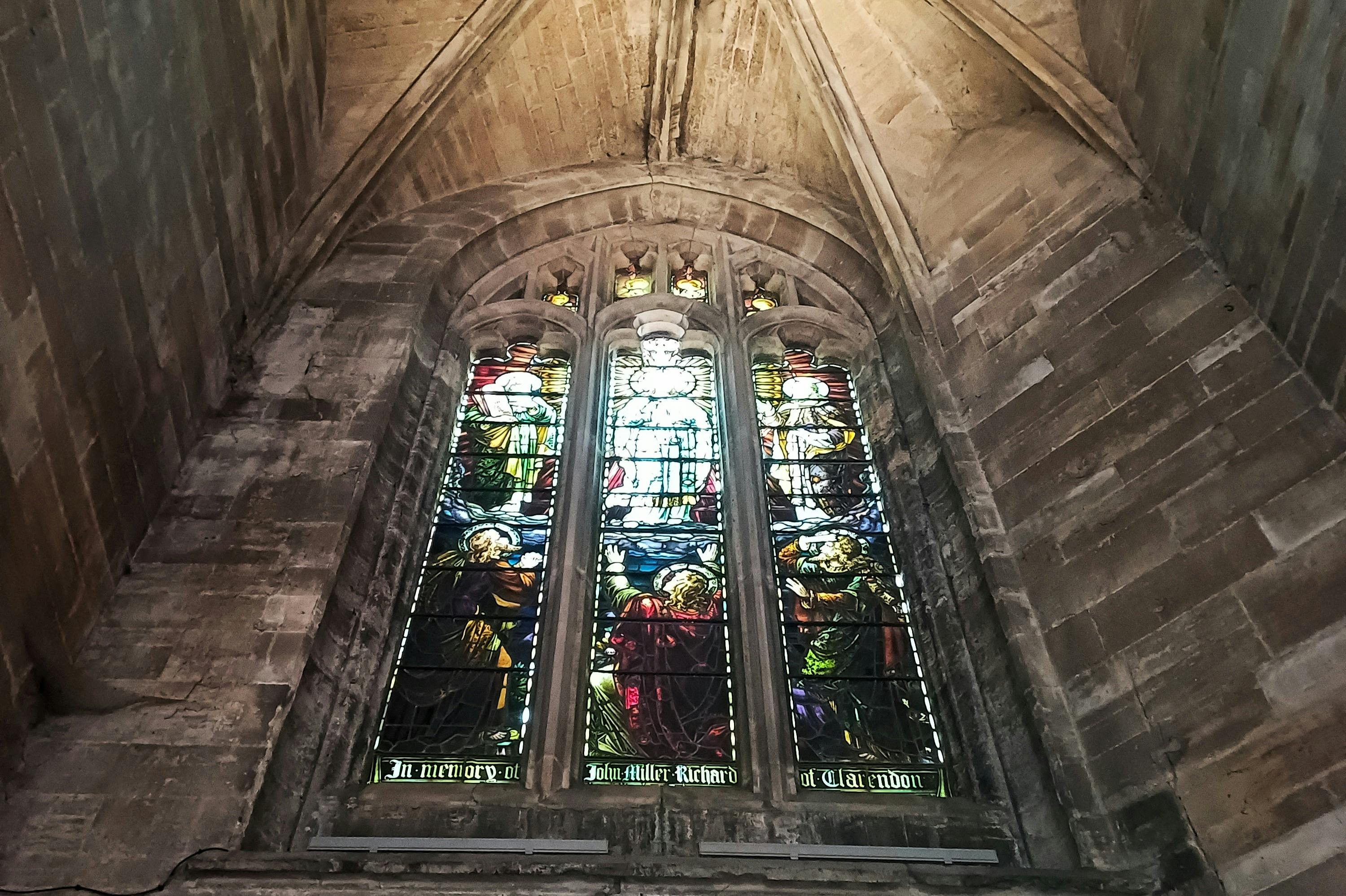 Большое витражное окно в церкви, изображающее красочные религиозные сцены, расположено в каменной готической арке.