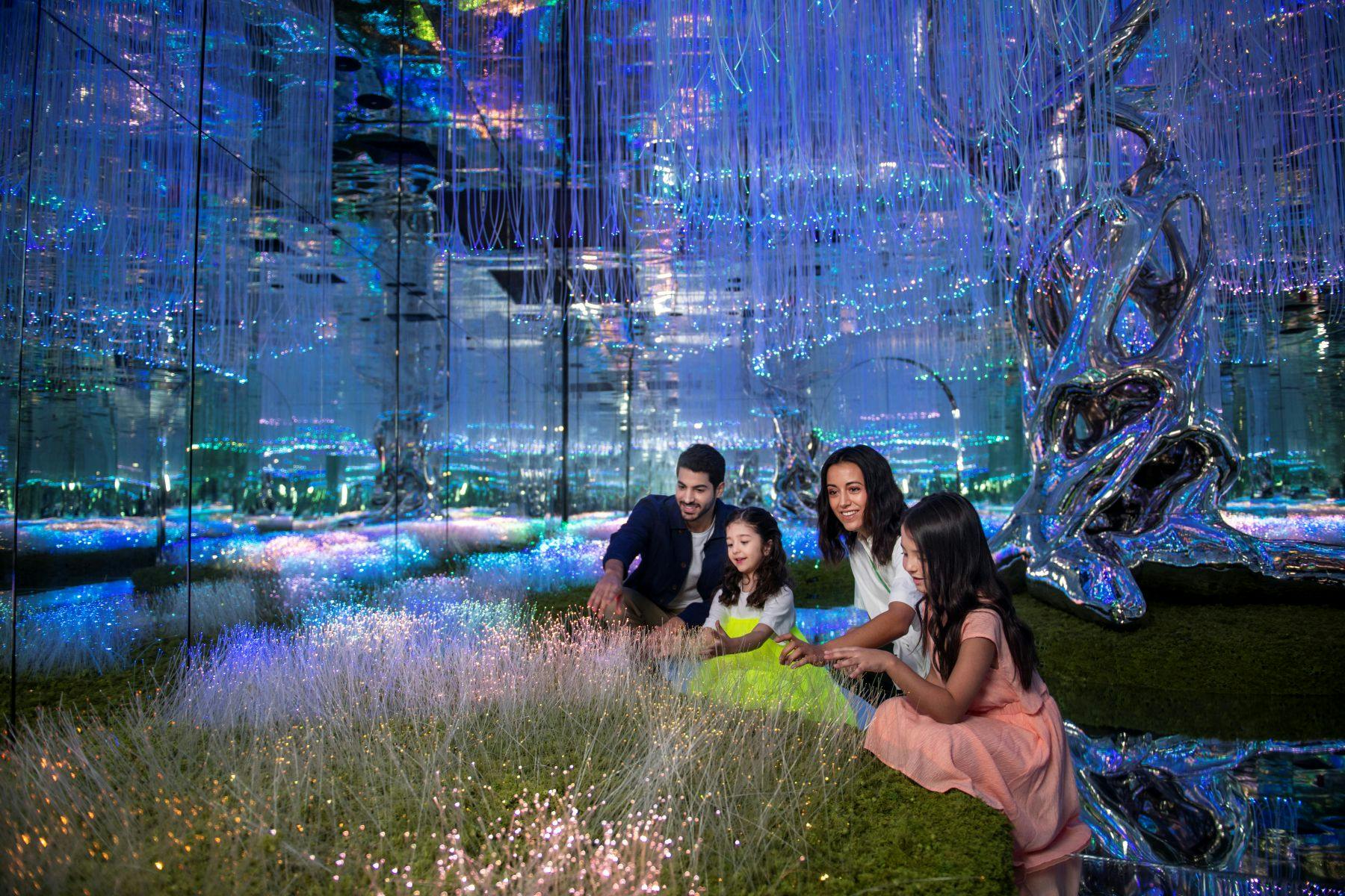 빛나는 조명과 미래 지향적인 인테리어가 돋보이는 반사 방의 녹색 표면에 앉아 있는 한 무리의 사람들.