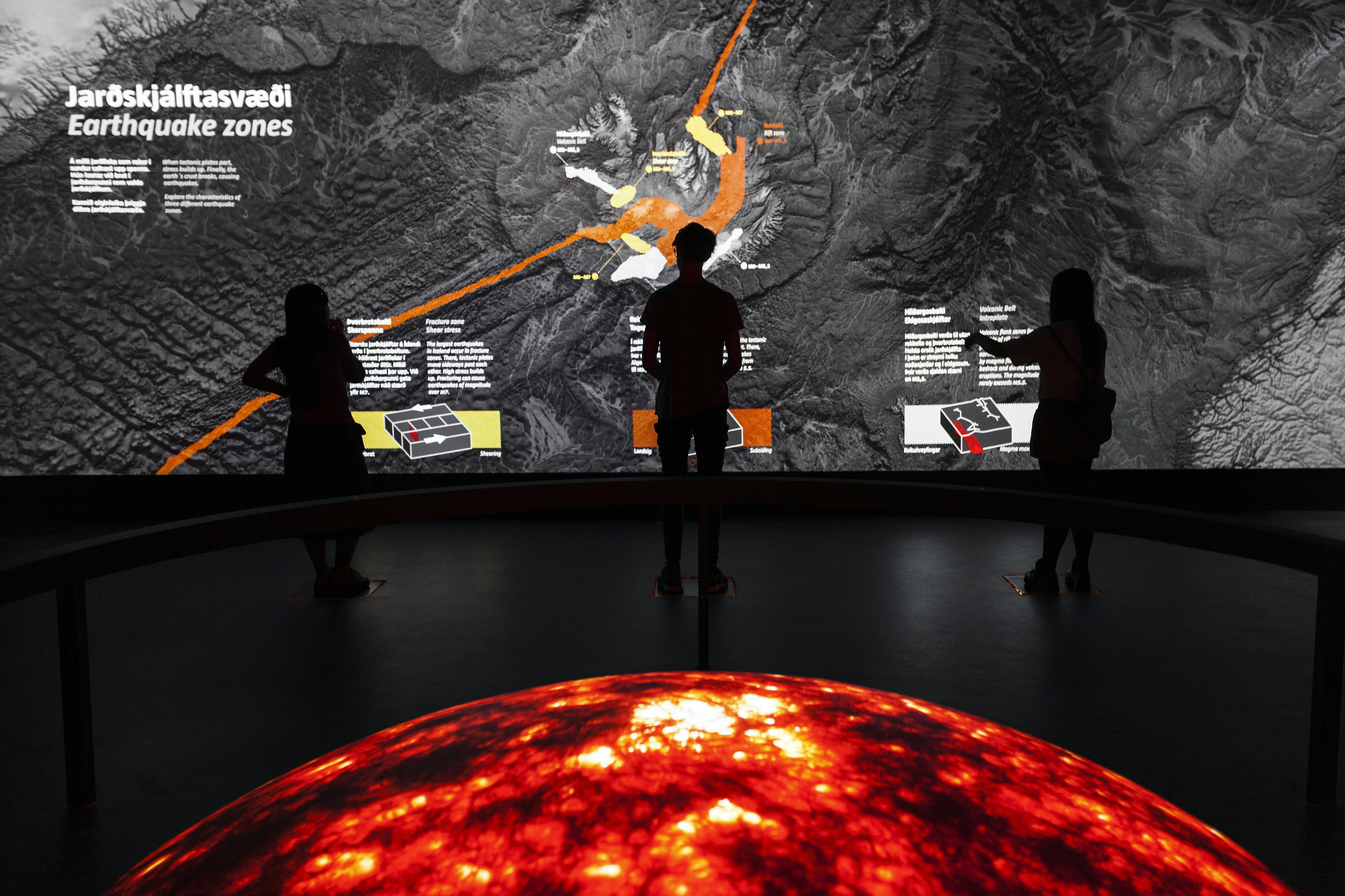 텍스트와 그래픽 요소가 있는 크고 밝은 지형도 앞에 세 사람이 서 있습니다. 눈부시게 빛나는 용암 같은 구체가 눈앞에 펼쳐집니다.