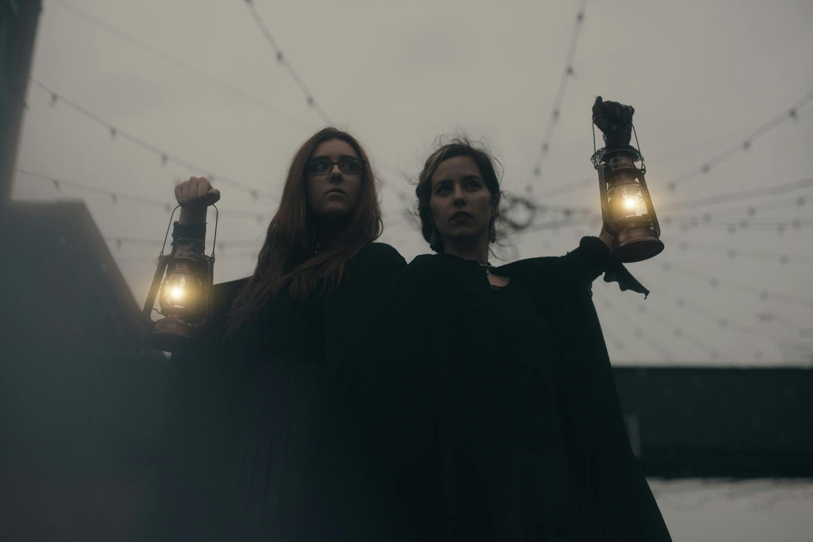 两个人在昏暗的室外环境中举着灯笼，上面有绳灯。 他们穿着深色衣服。