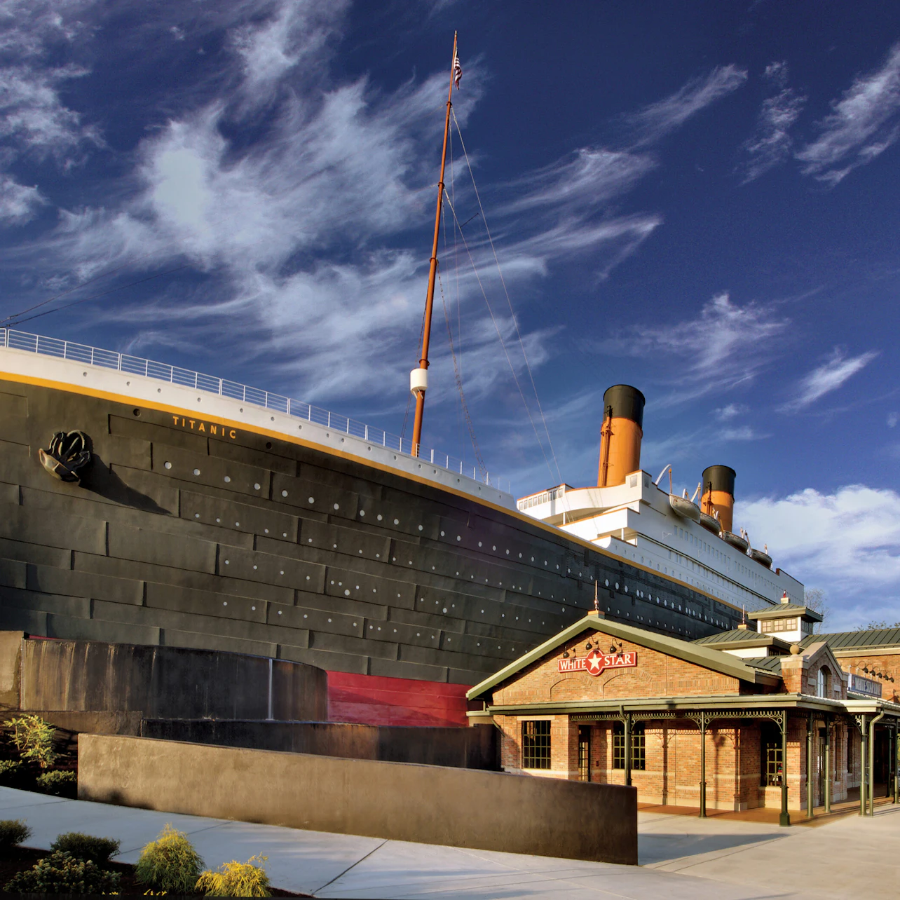 A building resembling the Titanic ship and a small brick structure with a "Titanic" sign, set against a blue sky with clouds.