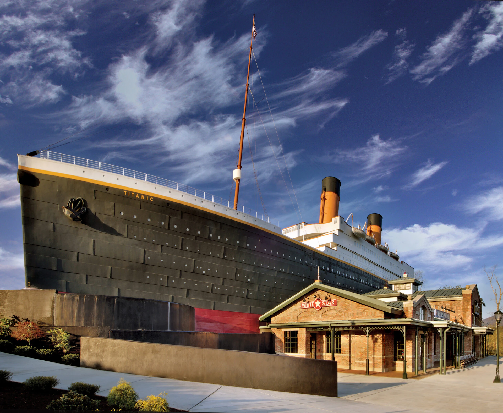 A building resembling the Titanic ship and a small brick structure with a "Titanic" sign, set against a blue sky with clouds.