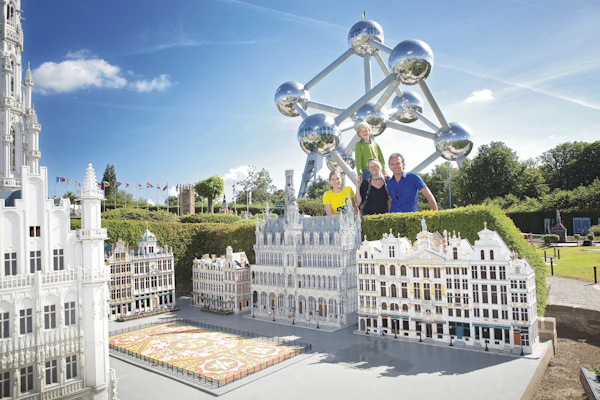 Quatre persones darrere de maquetes en miniatura d'edificis europeus amb l'estructura Atomium al fons en un dia assolellat.