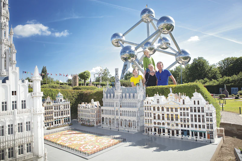 Quatre persones darrere de maquetes en miniatura d'edificis europeus amb l'estructura Atomium al fons en un dia assolellat.