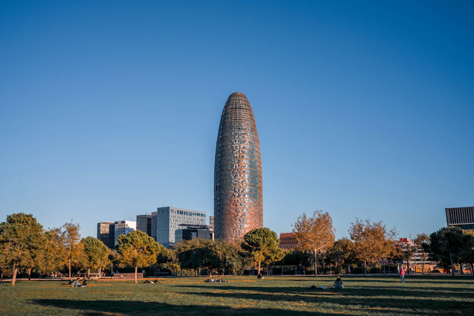 A cityscape with a tall, rounded building and trees in the foreground under a clear blue sky.