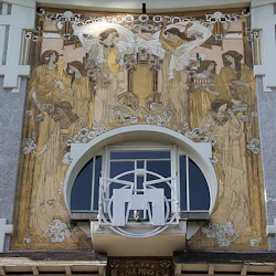 En detaljerad väggmålning med tio kvinnor omgivna av utsmyckade mönster, belägen runt ett stort fönster på en byggnadsfasad.