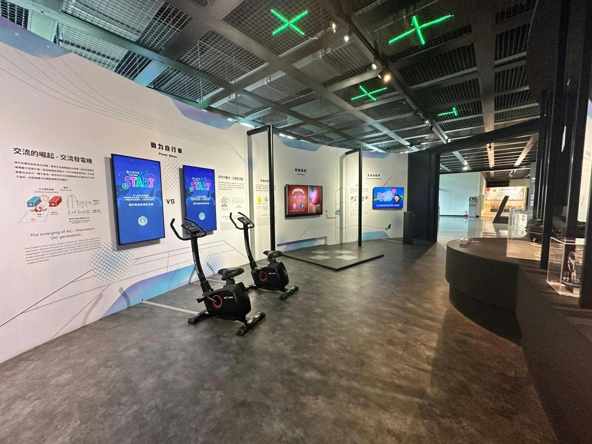 A modern indoor exhibition space featuring stationary exercise bikes in front of screens and informational displays.