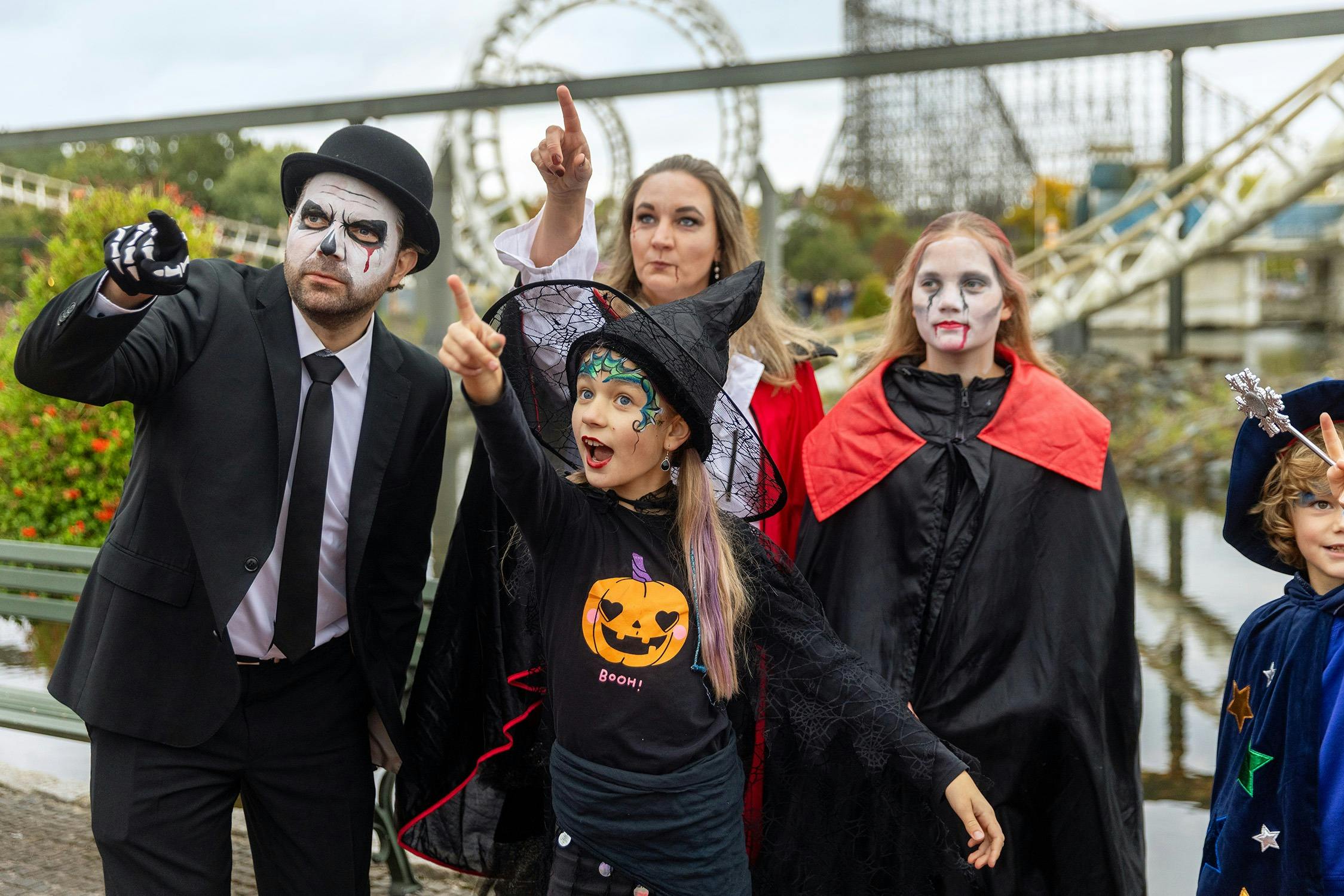 Un gruppo di bambini e adulti in costume di Halloween, tra cui una strega e un vampiro, che indicano qualcosa e guardano avanti.