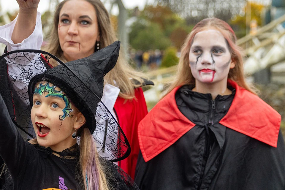 A group of children and adults in Halloween costumes, including a witch and a vampire, pointing and looking forward.