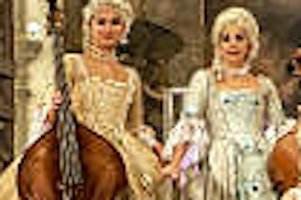 Group of people in elaborate period costumes, holding musical instruments, standing on a grand staircase of a luxurious building.