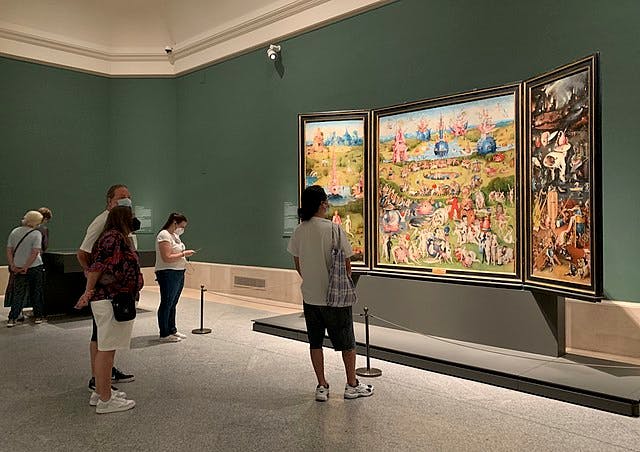Personnes regardant un tableau triptyque aux détails complexes dans une galerie d'art aux murs verts.