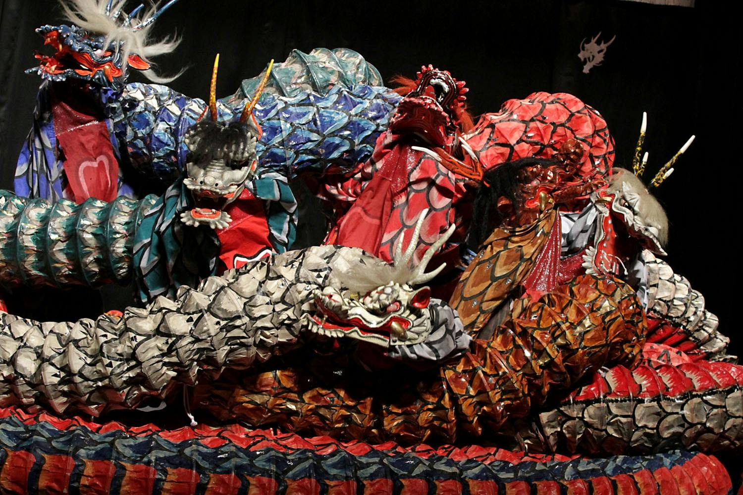 Elaborately decorated snake-like dragon costumes in vibrant colors displayed on a stage, with intricate patterns and details.