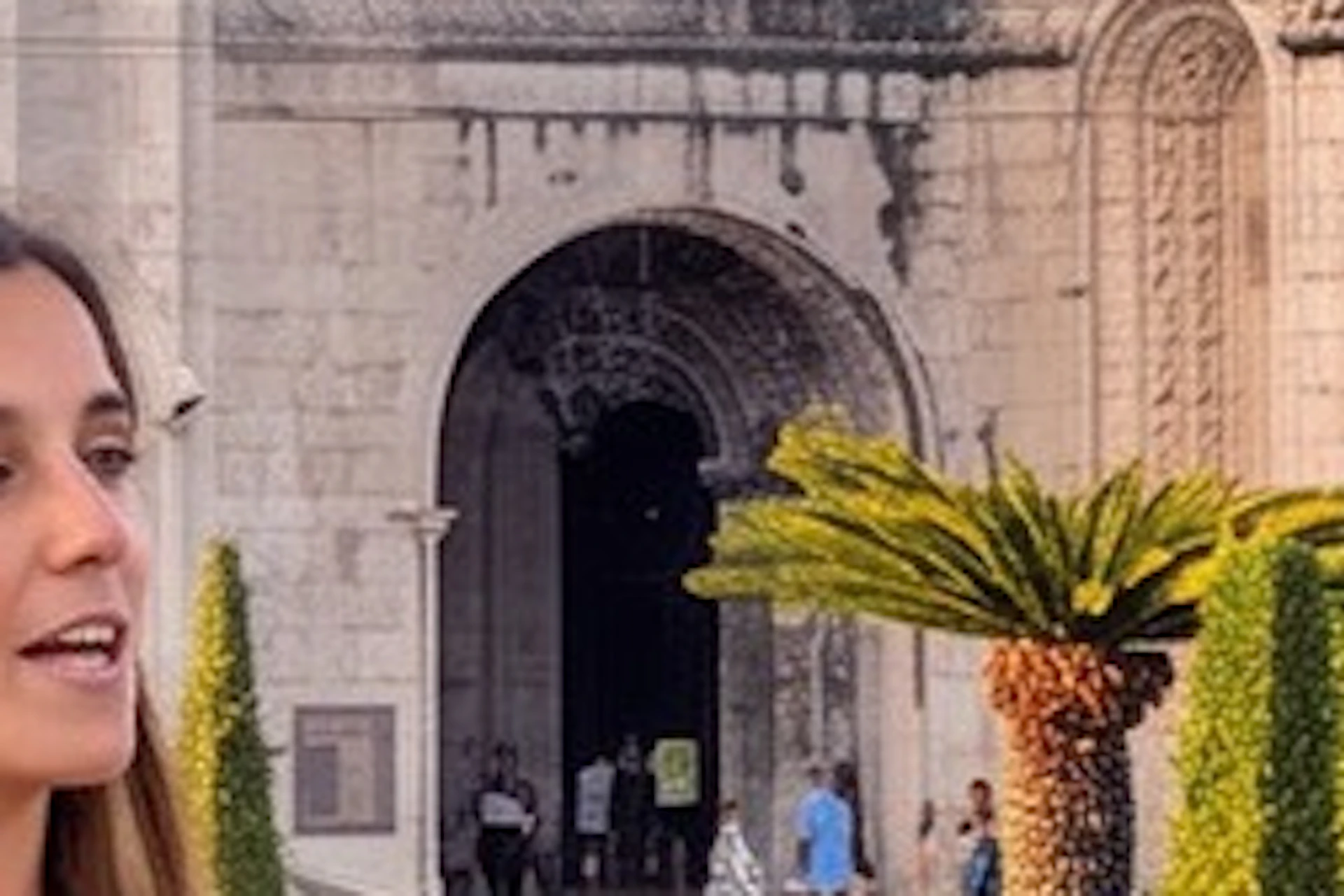 A group of people interacts with a guide near a historic building surrounded by gardens during sunset.
