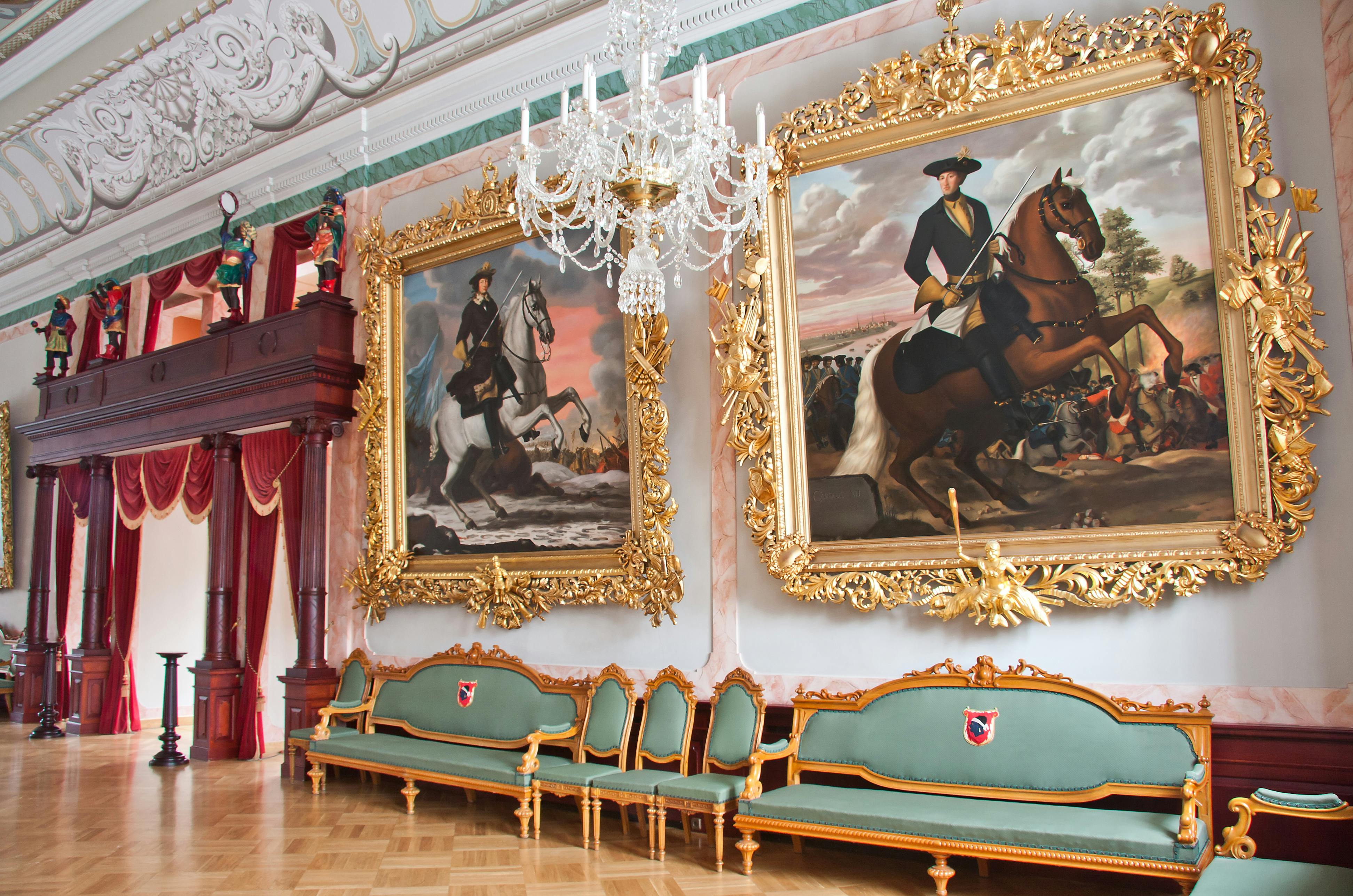 这间宽敞的房间配有两幅大型华丽的马画、绿色沙发、带金色装饰的椅子和吊灯。