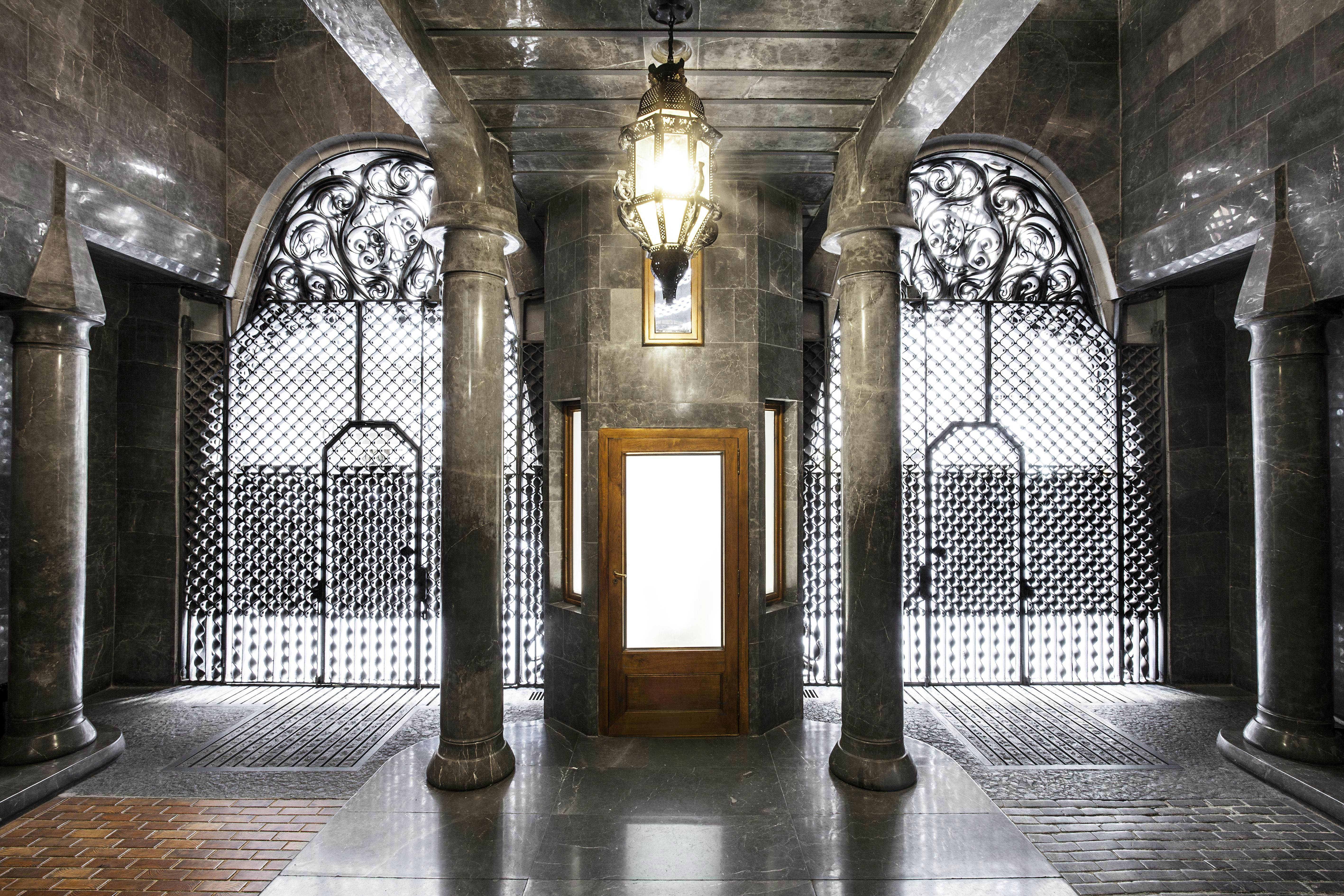 Hallway with marble columns, an ornate chandelier, a wooden door, and decorative metal gates on both sides.