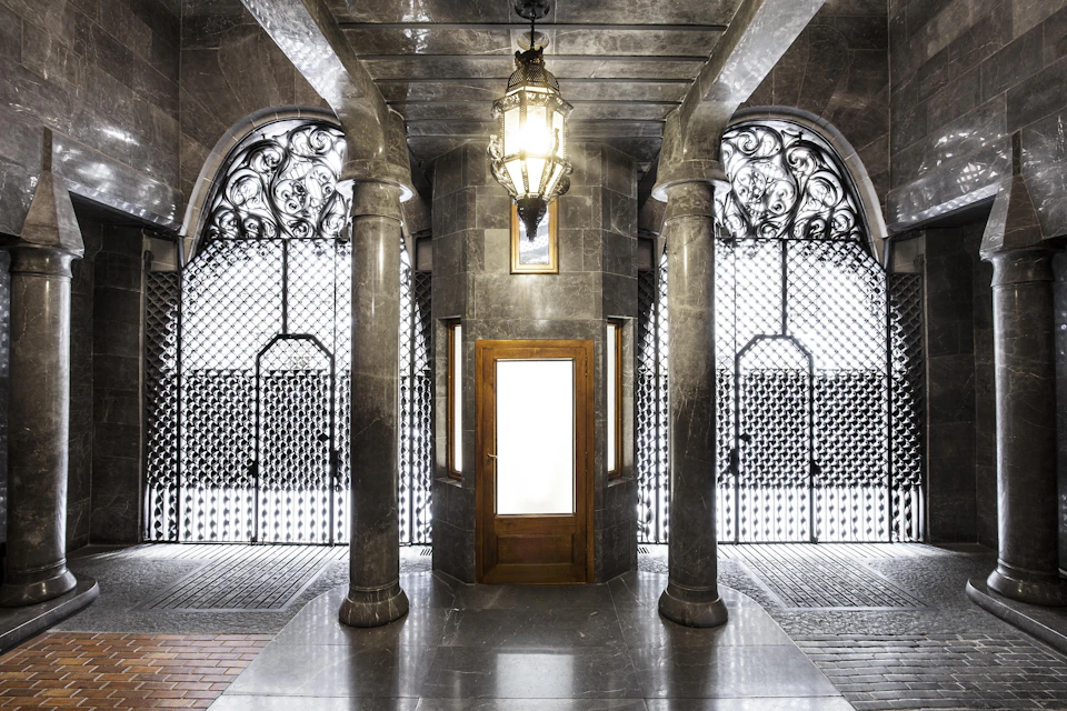 Hallway with marble columns, an ornate chandelier, a wooden door, and decorative metal gates on both sides.