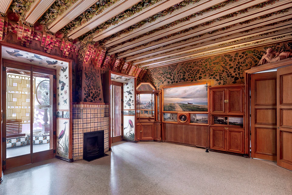 Ornate room with floral and bird-themed decor, wooden cabinets, a fireplace, large windows, and a landscape painting.