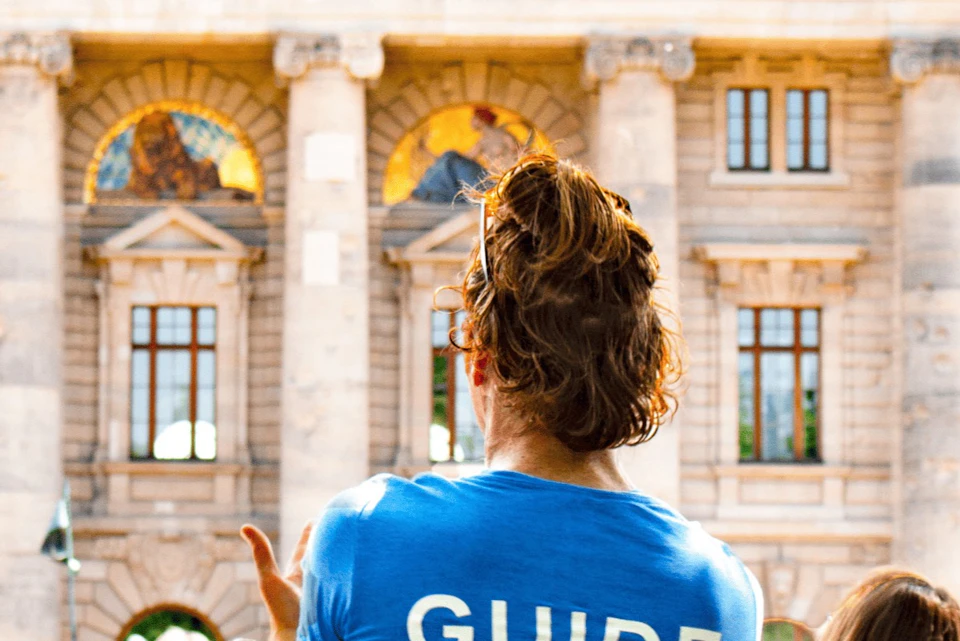 A person wearing a blue shirt with "GUIDE" written on the back, standing in front of a historical building with arched windows.