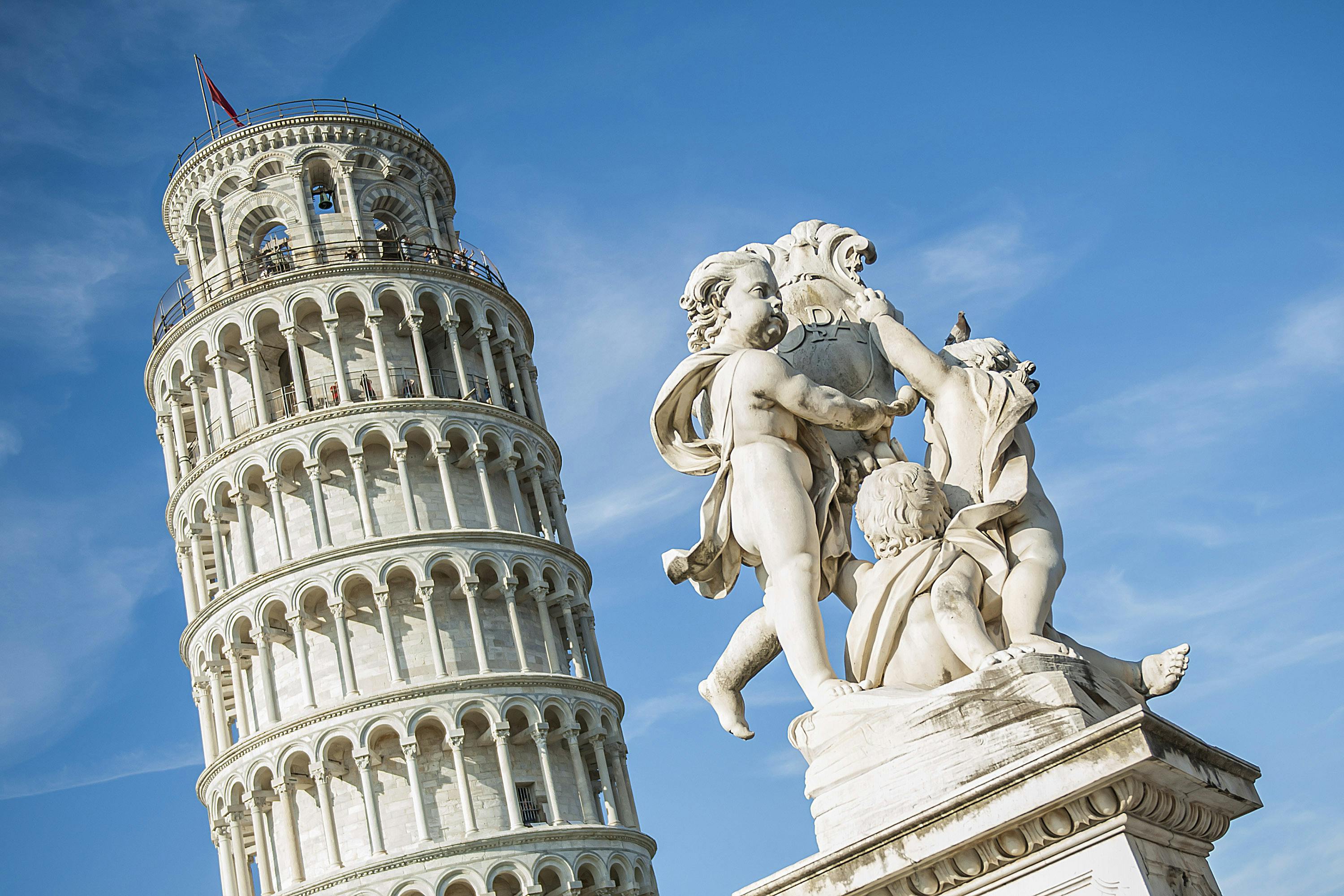 比萨斜塔（ Leaning Tower of Pisa ）前有三个小天使的白色大理石雕像，晴朗的蓝天下。