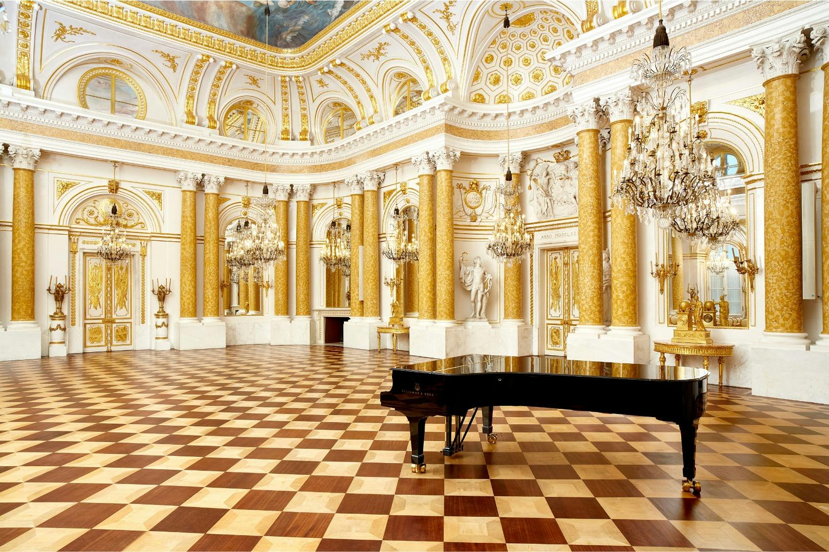 Prunkvolle Halle mit goldenen Säulen, Kronleuchtern, Marmorakzenten, einem karierten Boden und einem Flügel im Vordergrund.