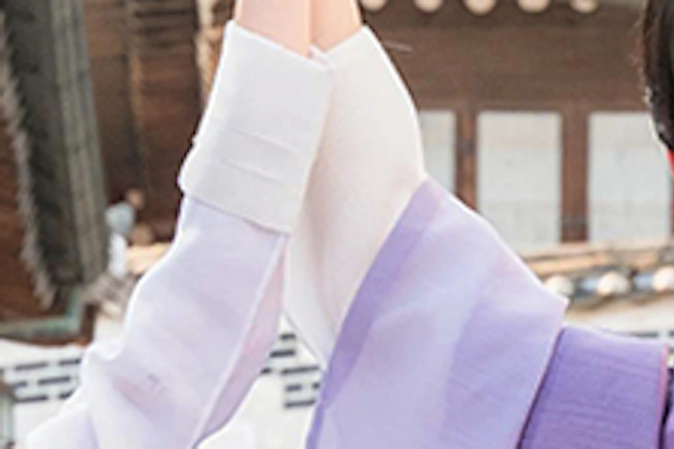 A man and woman in traditional Korean hanbok pose on a street in a traditional village setting.