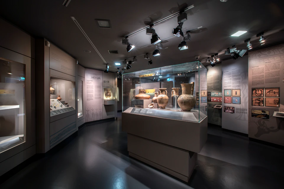 A museum exhibit featuring ancient pottery displayed in a glass case, with informational panels and spotlights above.
