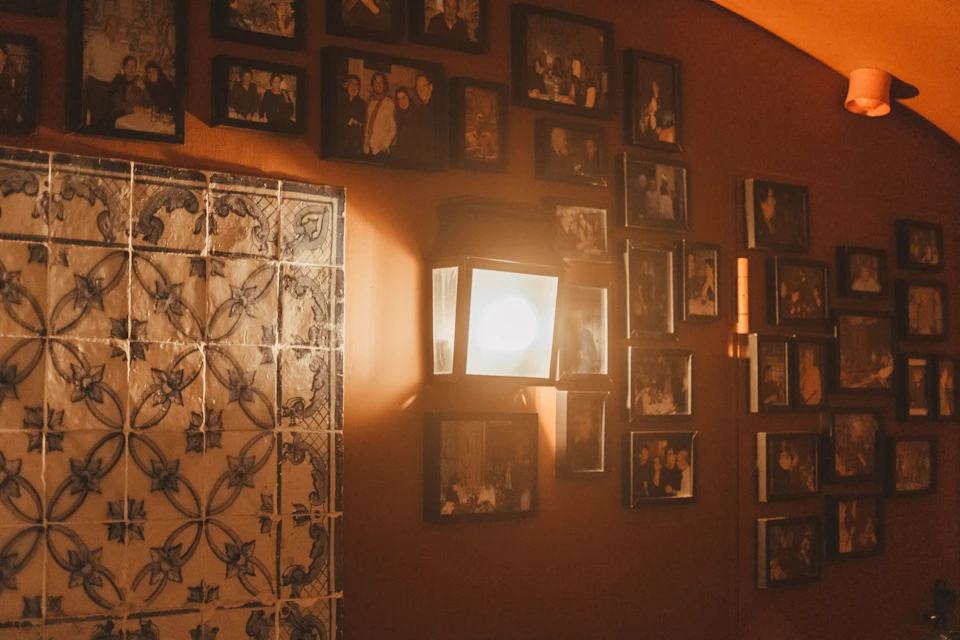 A wall-mounted lamp illuminates framed photos and decorative tiles on an orange wall.