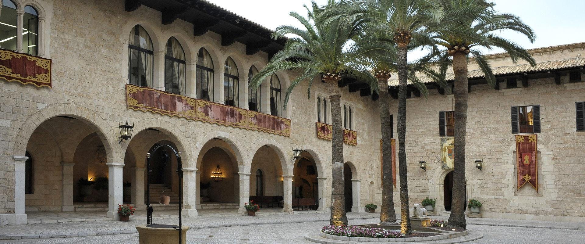 石头庭院，有拱形人行道，楼上阳台有装饰品、棕榈树和盆栽植物。