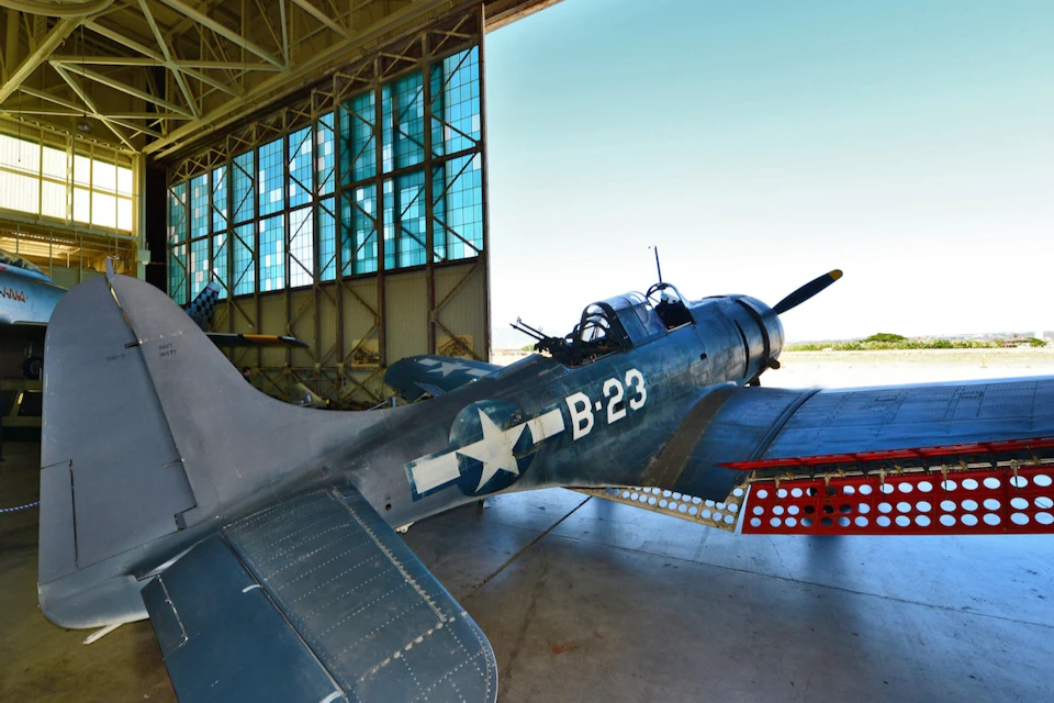 A WWII-era warplane labeled "B-23" with a star insignia is parked in an open-air hangar with large windows.