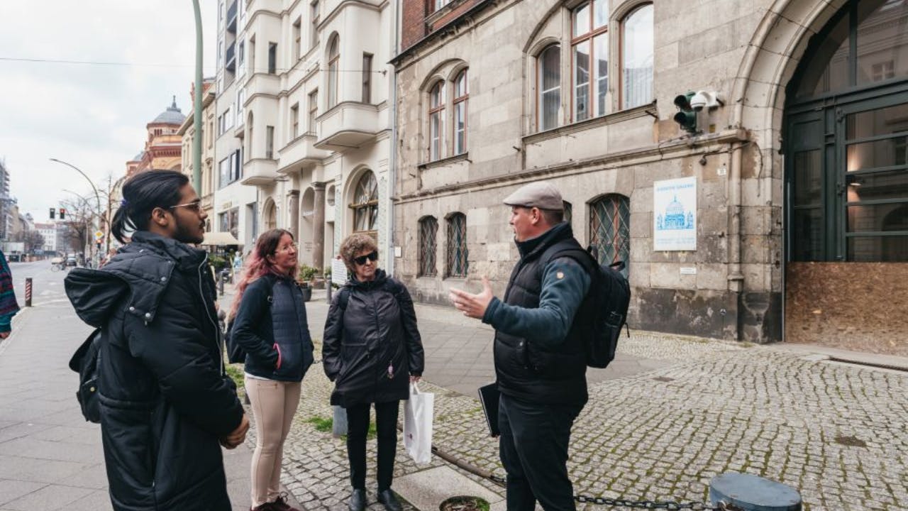 A group of four people, dressed in winter clothing, standing and talking on a city street lined with buildings.