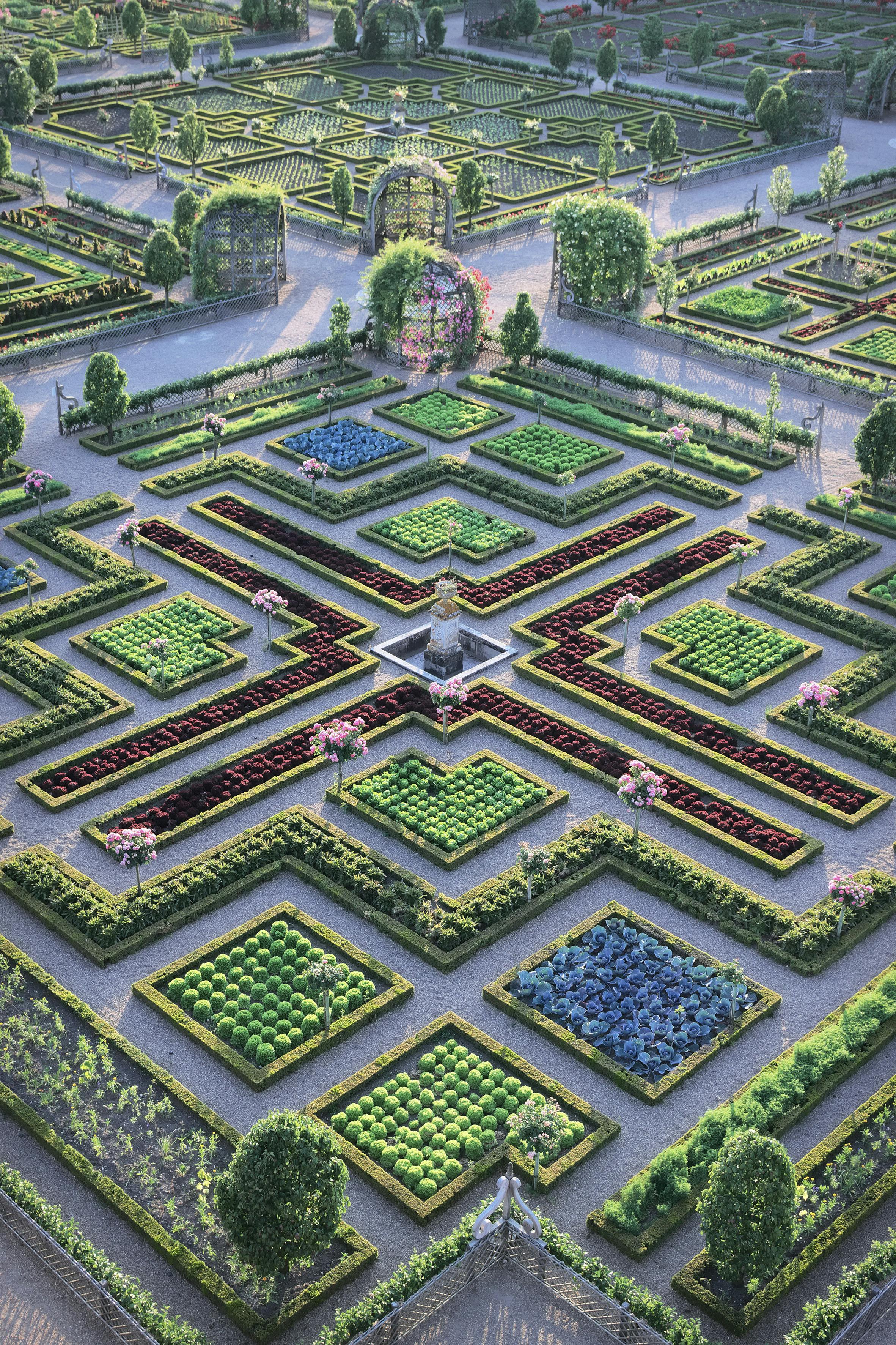 Un giardino formale simmetrico con siepi intricate e ben curate, aiuole colorate e un punto focale centrale.