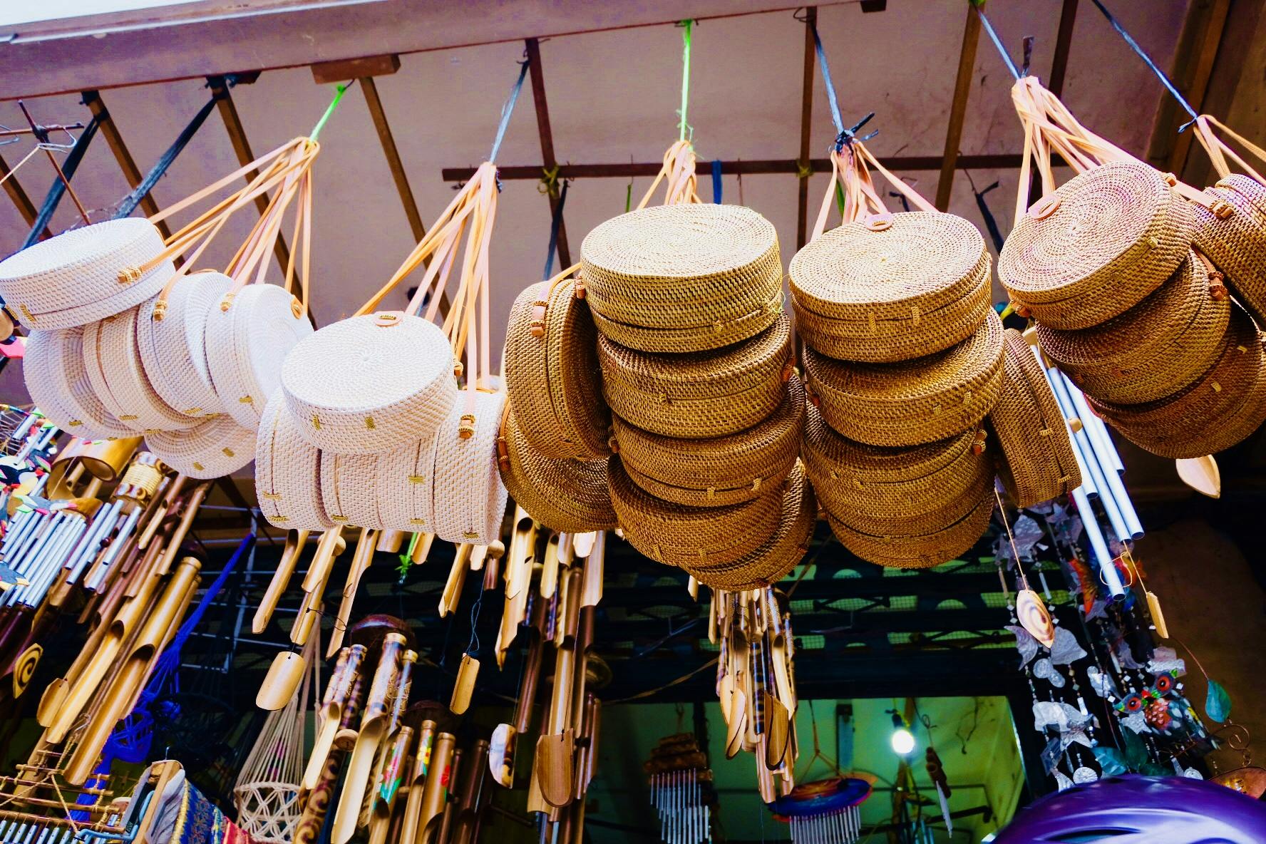 Straw and wicker hats, fans, and ornaments hang from the ceiling in a market stall.