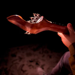 Närbild av en person som stämmer en gitarr i svag belysning och markerar instrumentets nacke och stämmare.