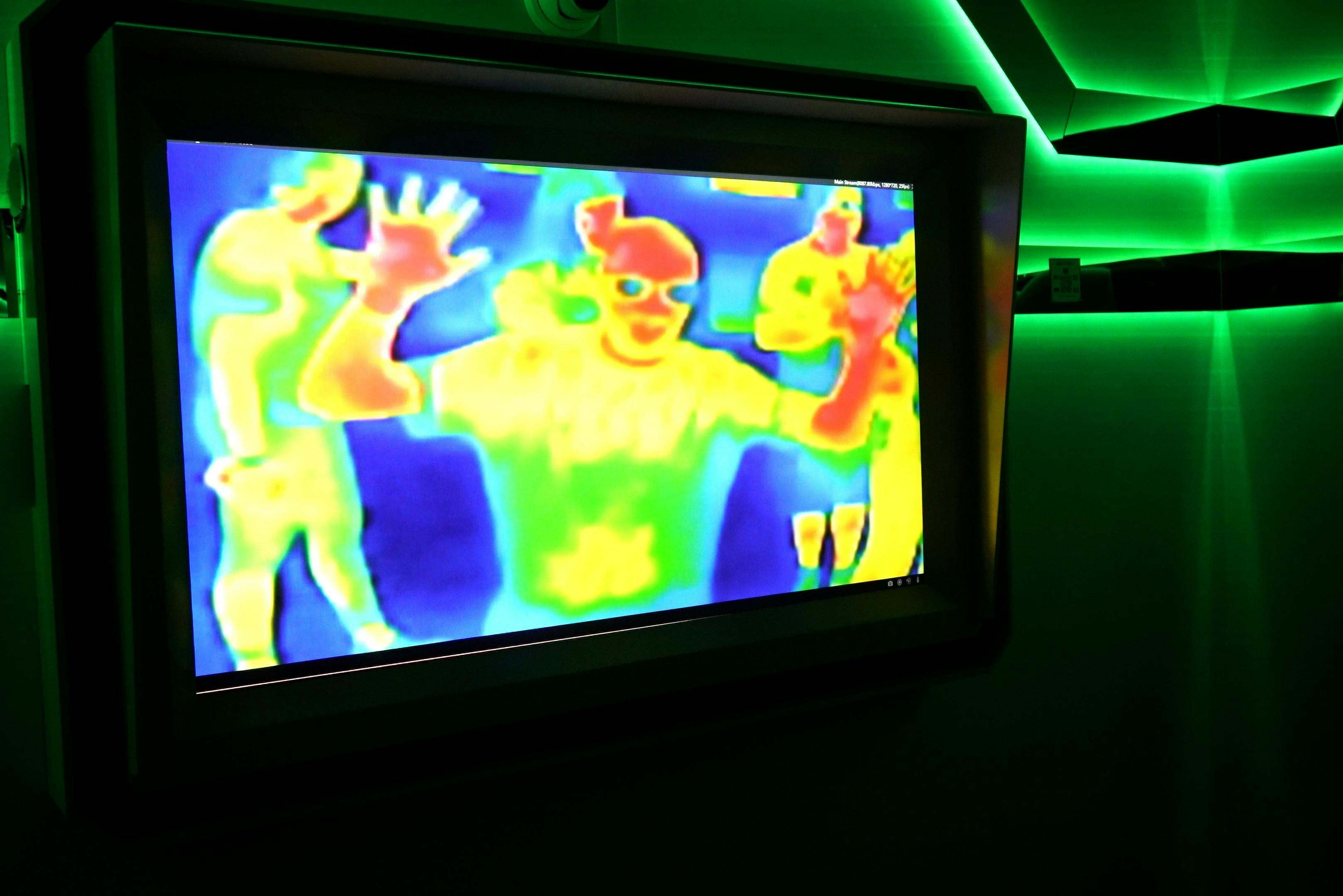 屏幕上显示的热图像，显示绿色环境照明的房间中人们的彩色热特征。