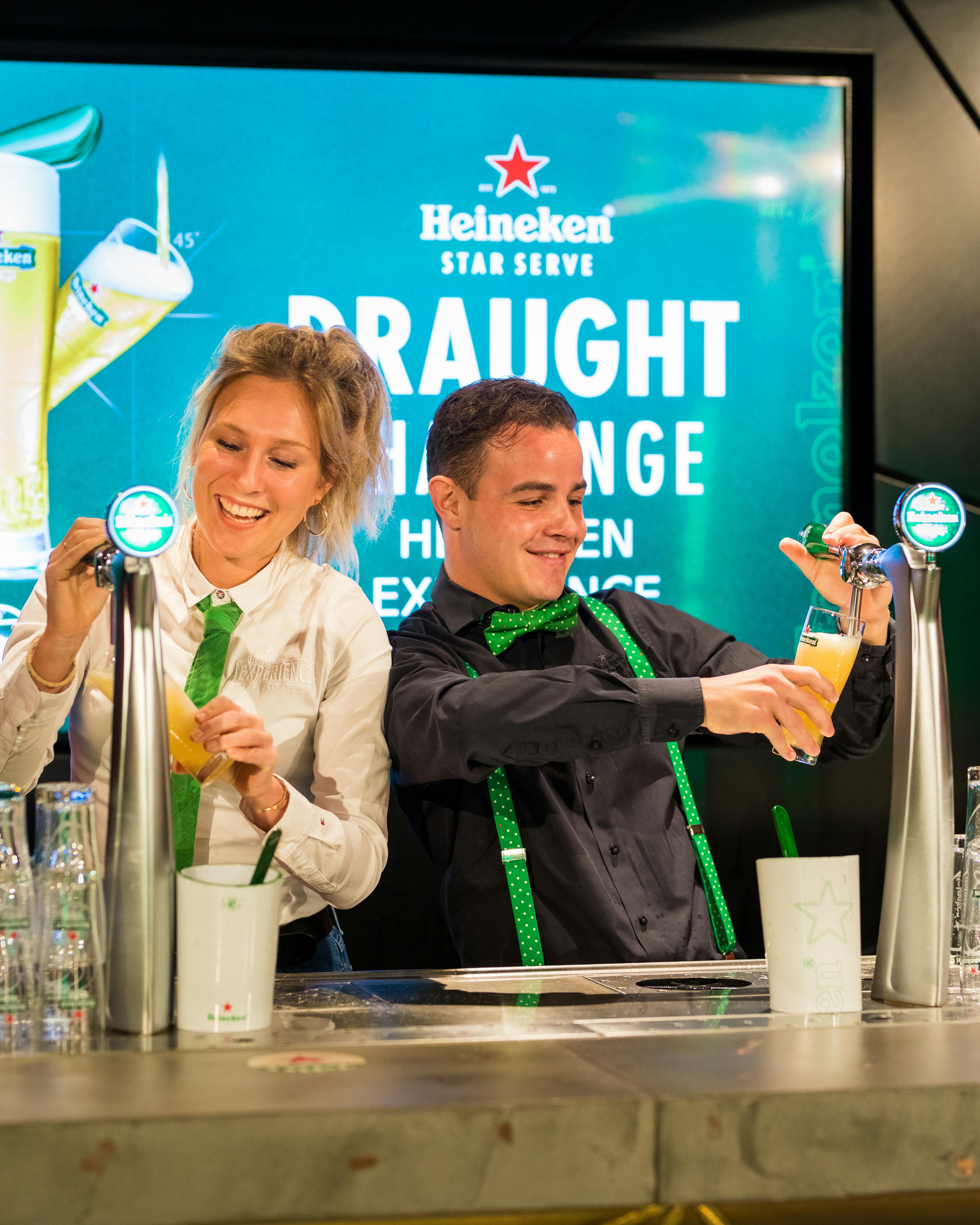 酒吧里有两个人微笑着倒啤酒，背景是喜力品牌。