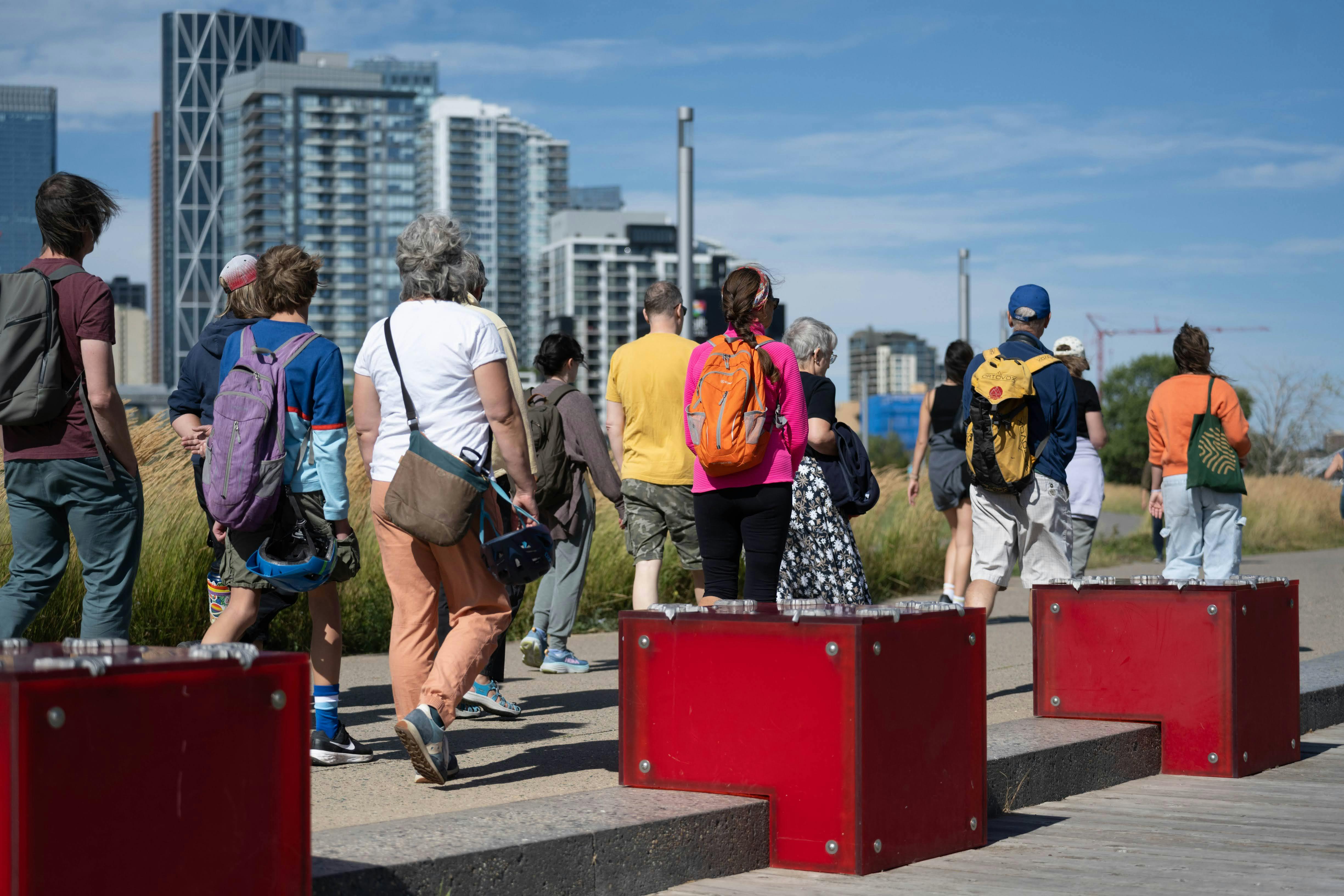 Group of people walking outdoors with backpacks, surrounded by city buildings and red blocks.