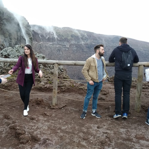 Four people stand on a rocky path with a wooden railing, overlooking a mountainous landscape with mist and steep cliffs.