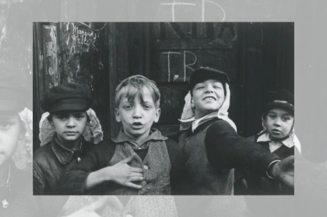 A black-and-white photo of three boys, one with outstretched arm, standing in front of a dark graffiti-covered wall.