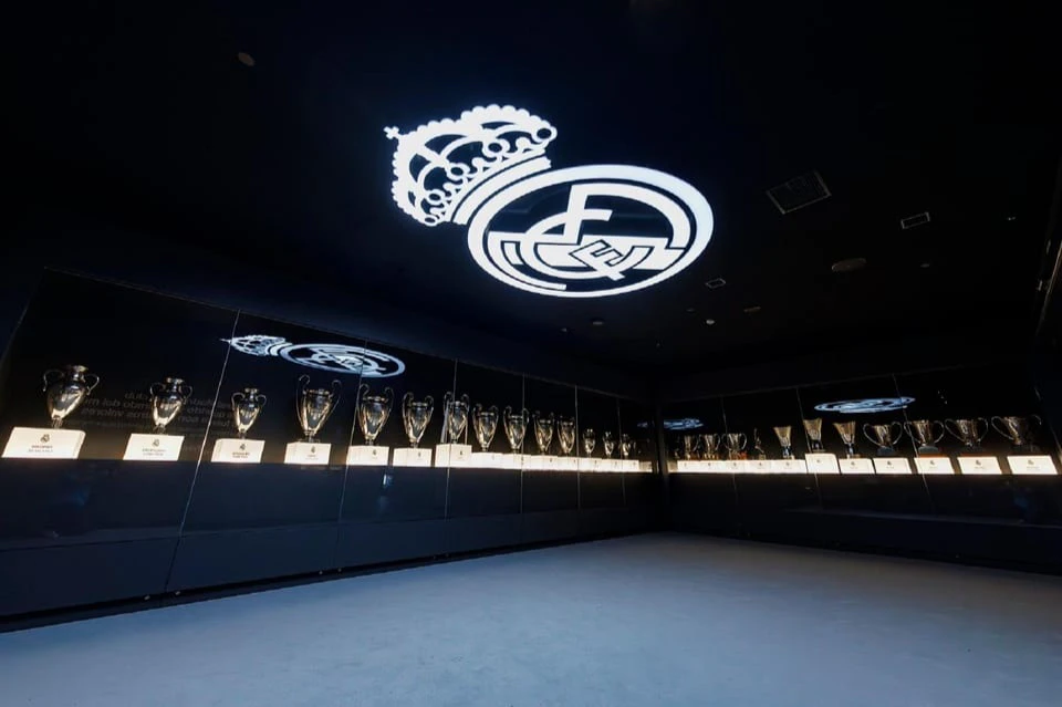 Room displaying numerous trophies, with a large illuminated crest on the ceiling and reflective walls.